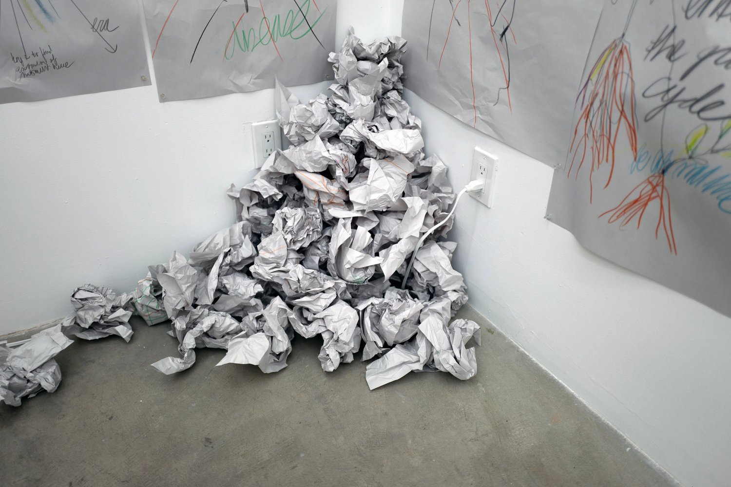Crumpled drawings piled in a corner below sheets pinned to the gallery walls.