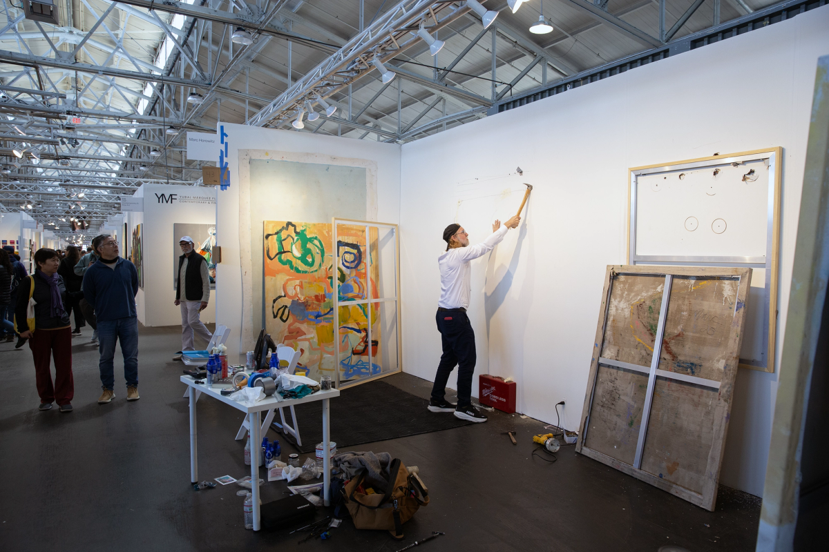 Marc hanging and rehanging paintings as visitors watch at San Francisco Art Fair.