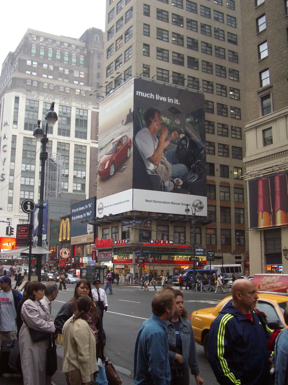 A large Nissan campaign billboard showing Marc eating inside a Sentra above a busy city street.