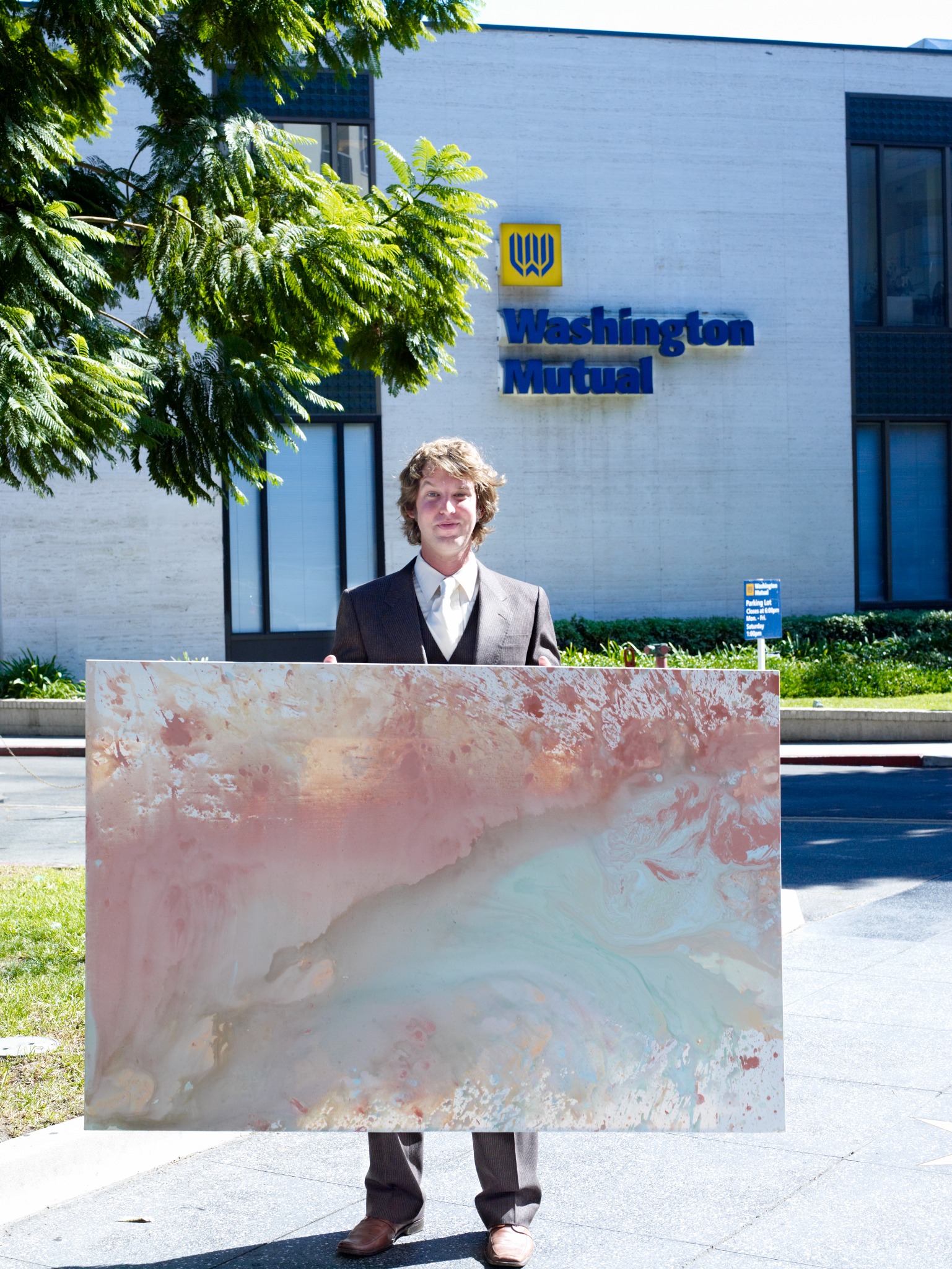Marc in a suit holding a finished painting outside a Washington Mutual bank.