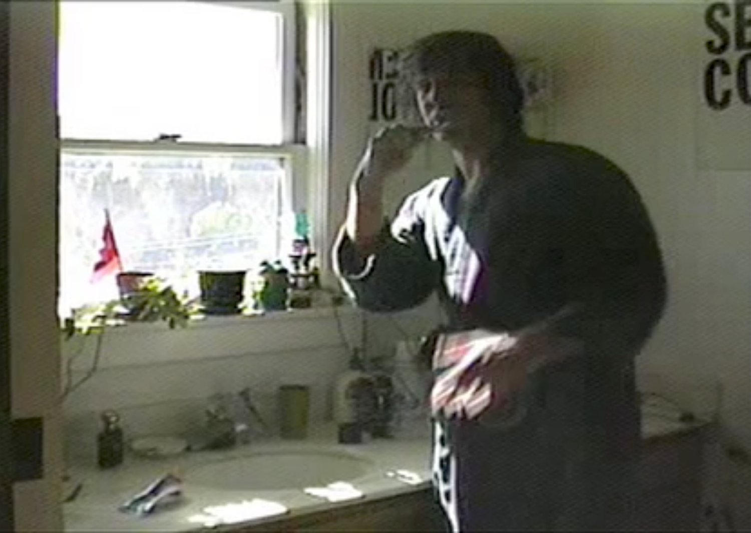 A low-resolution broadcast view of Marc holding a microphone beside a kitchen window.