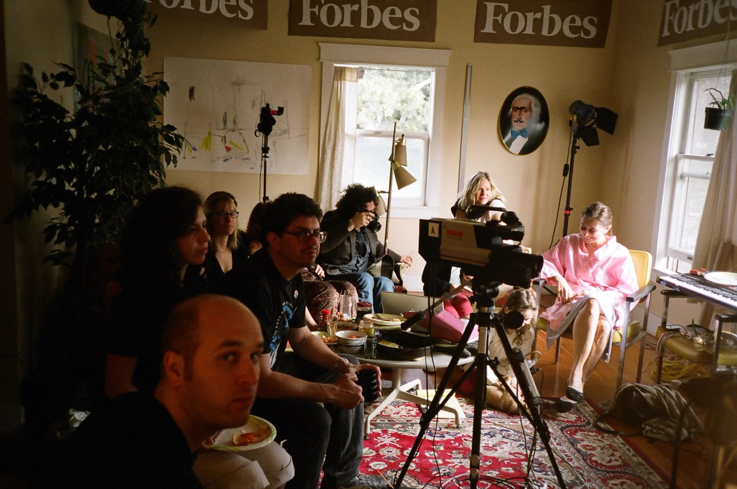Visitors gather in a living room around a camera on a tripod during Talkshow 24/7.